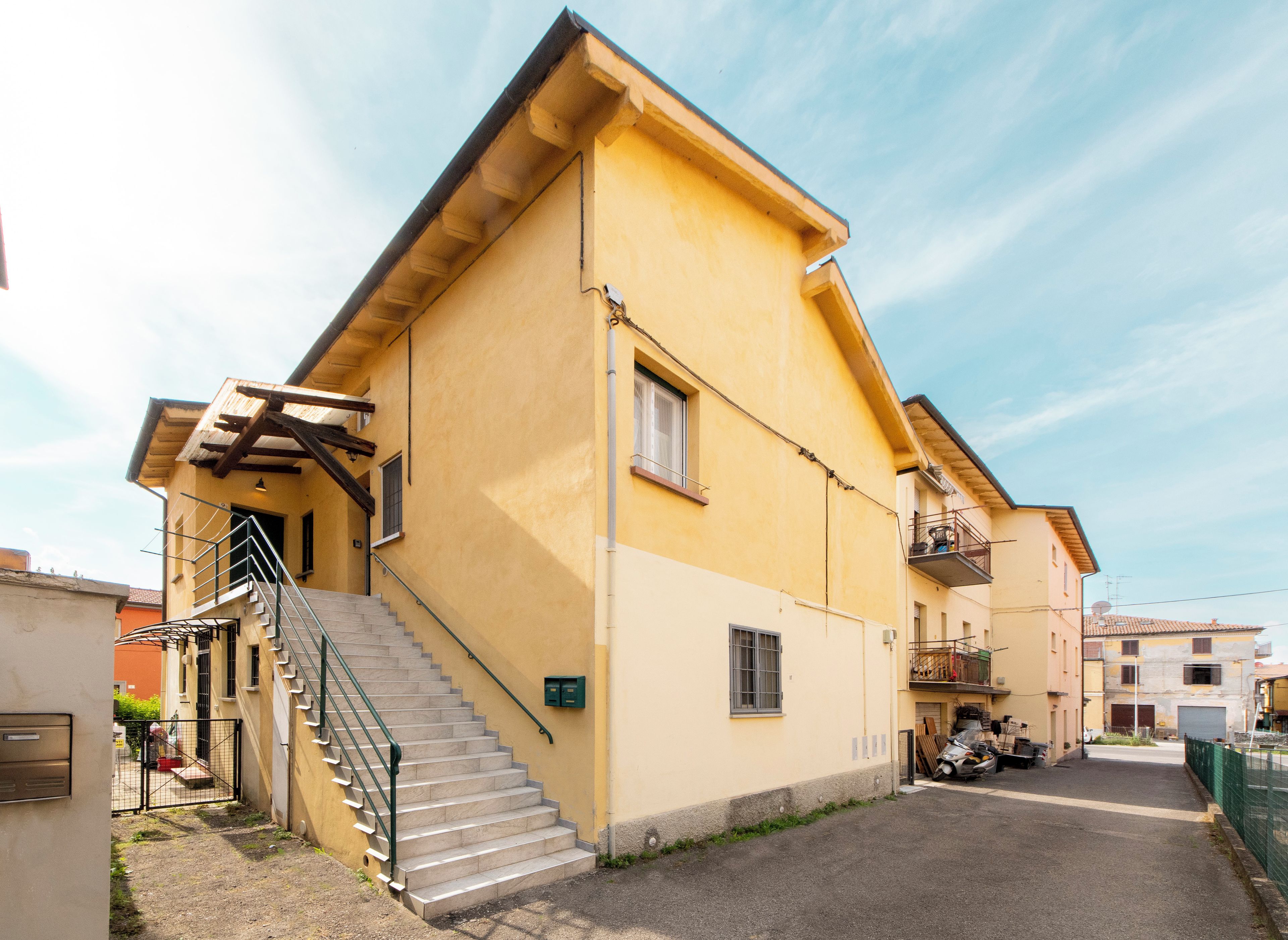 A yellow building with a staircase leading to a door, a small balcony, and a parked motorcycle.