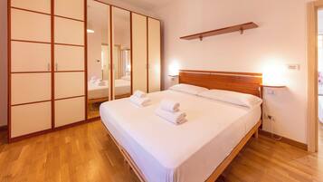 A hotel room with a bed, wooden flooring, a wardrobe with sliding doors, and a bedside table with a lamp.