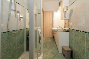 A bathroom with a glass shower enclosure, a toilet, a sink with a mirror, and a trash bin. - HouSmart Risorgimento 9 (Riale)