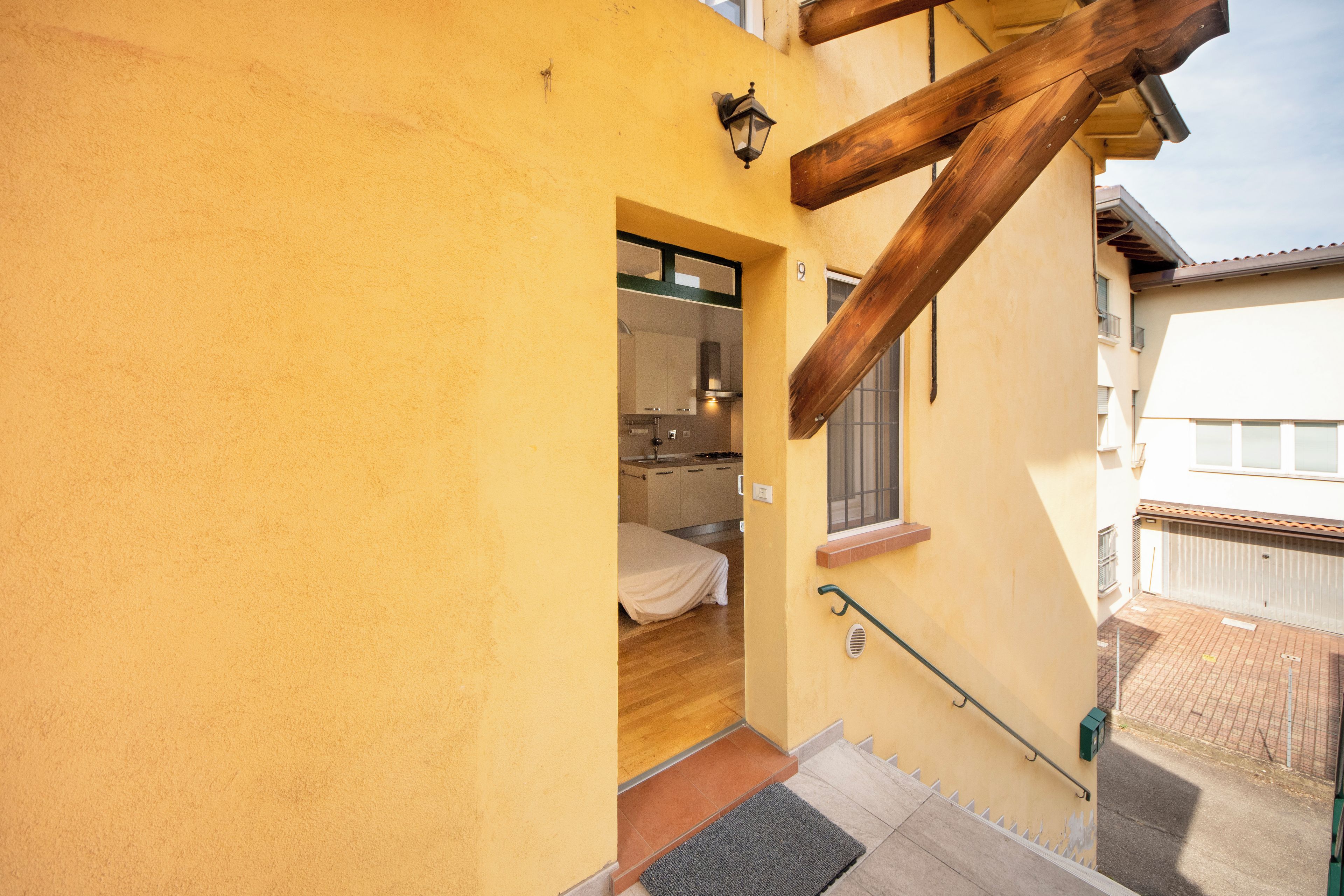 A yellow building with a wooden staircase leading to a room with a bed and a window.
