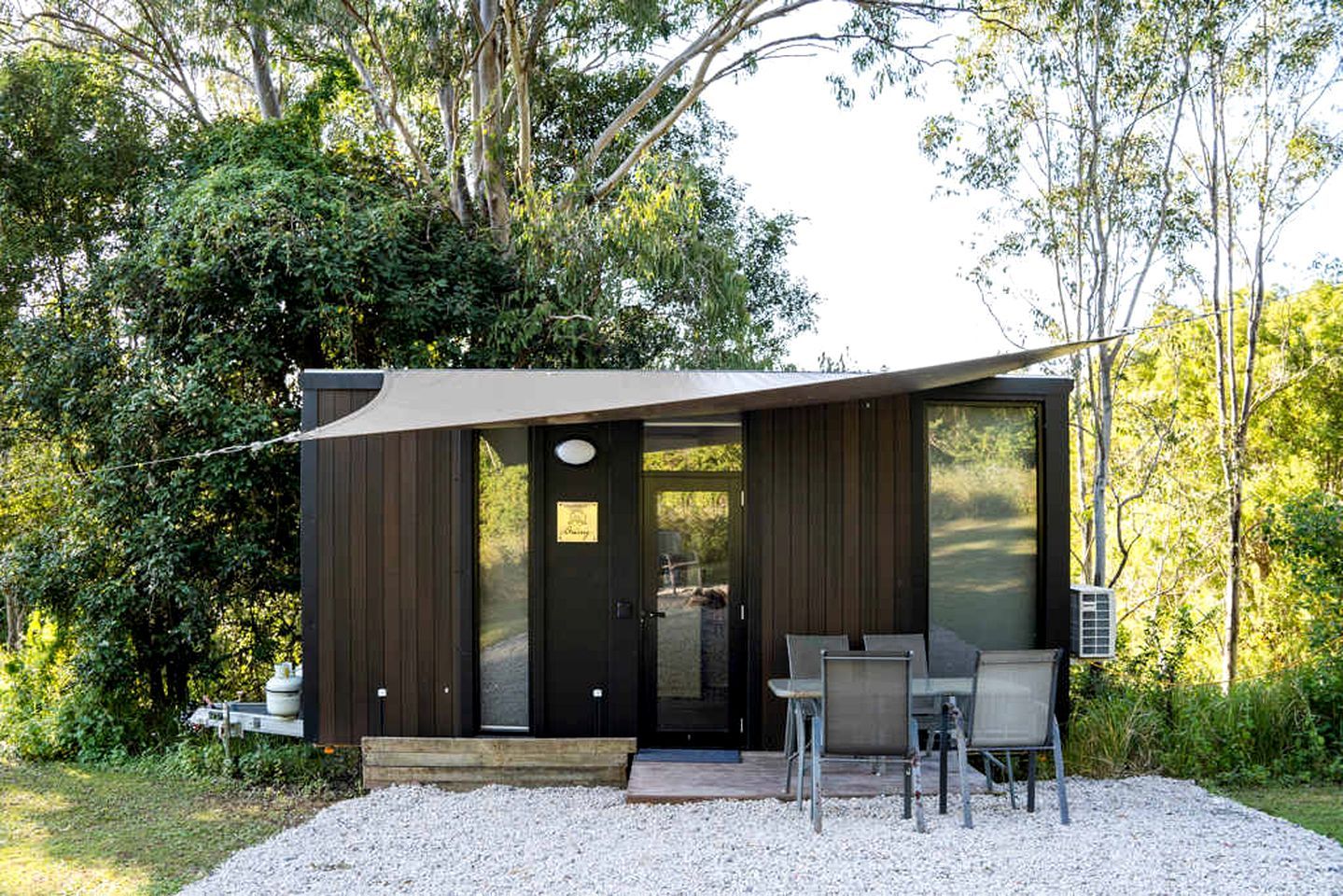 Une cabane moderne à l’extérieur sombre, dotée d’une grande porte-fenêtre coulissante et d’un espace patio avec des sièges d’extérieur.