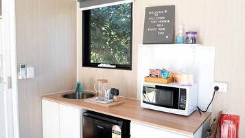 A compact kitchen with a sink, a microwave, and a small refrigerator. There's a window above the sink, and a welcome sign on the wall.