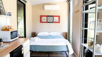 A compact hotel room with a bed, bedside tables, a microwave, a small kitchen area, and a view through the window.