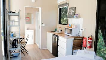 A compact hotel room with a kitchenette, a bed, a desk, and a chair.