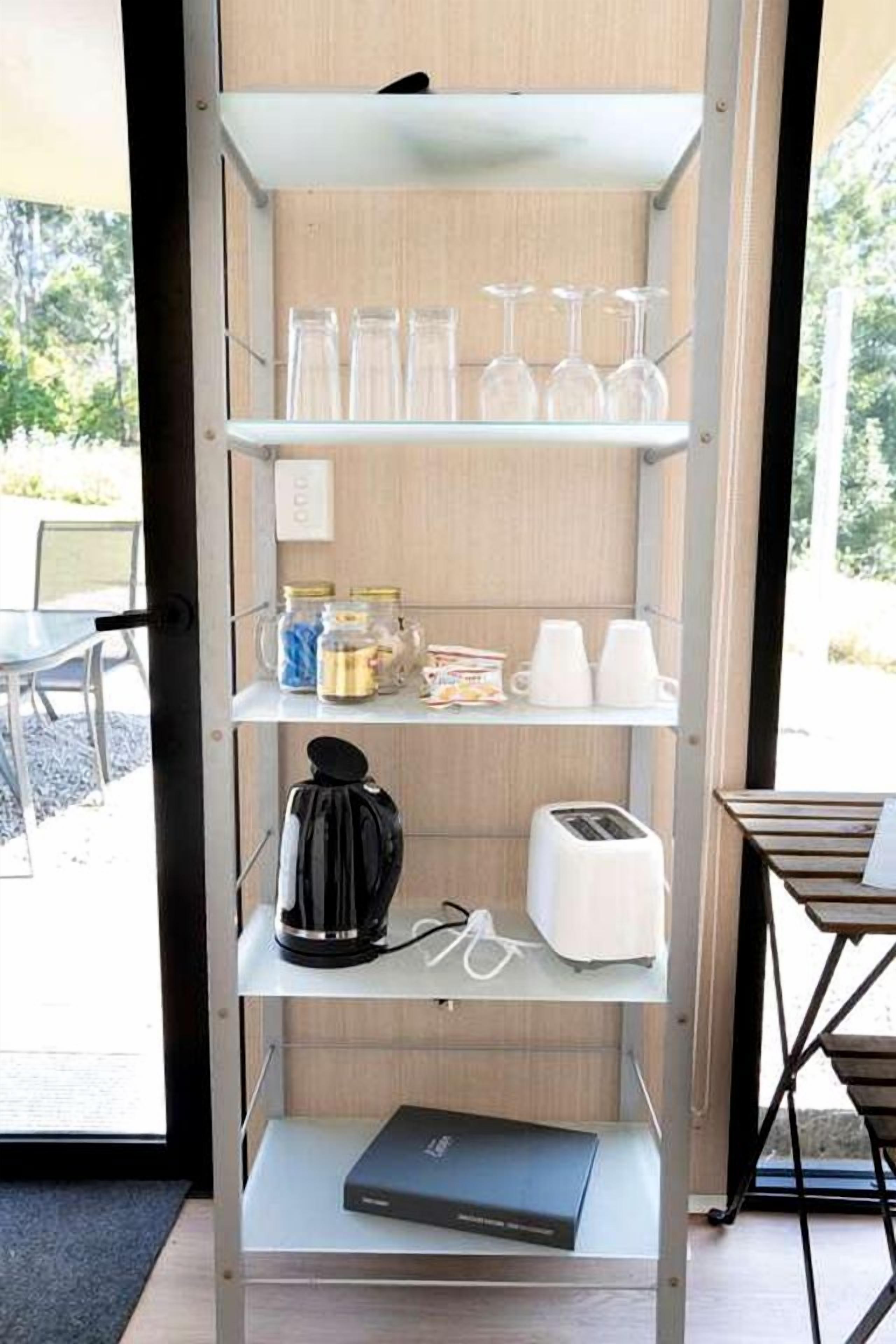 Un mueble con vajilla, una cafetera, un tostador y una computadora portátil.