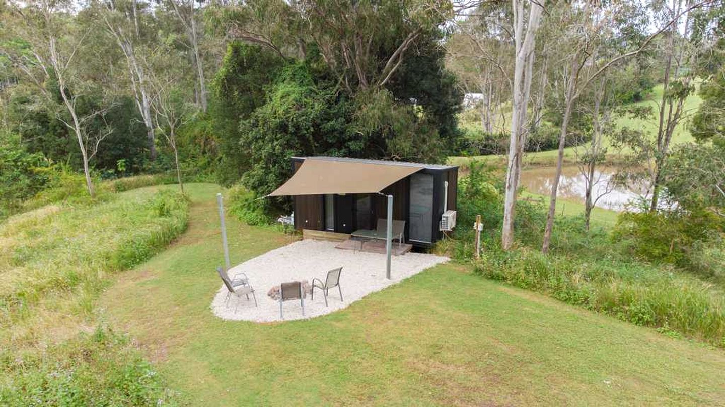 A secluded cabin with a patio, surrounded by trees and a body of water.