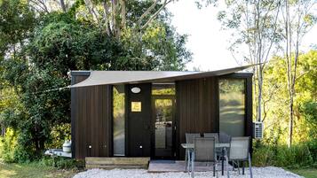 A modern cabin with a dark exterior, a large sliding glass door, and a patio area with outdoor seating.