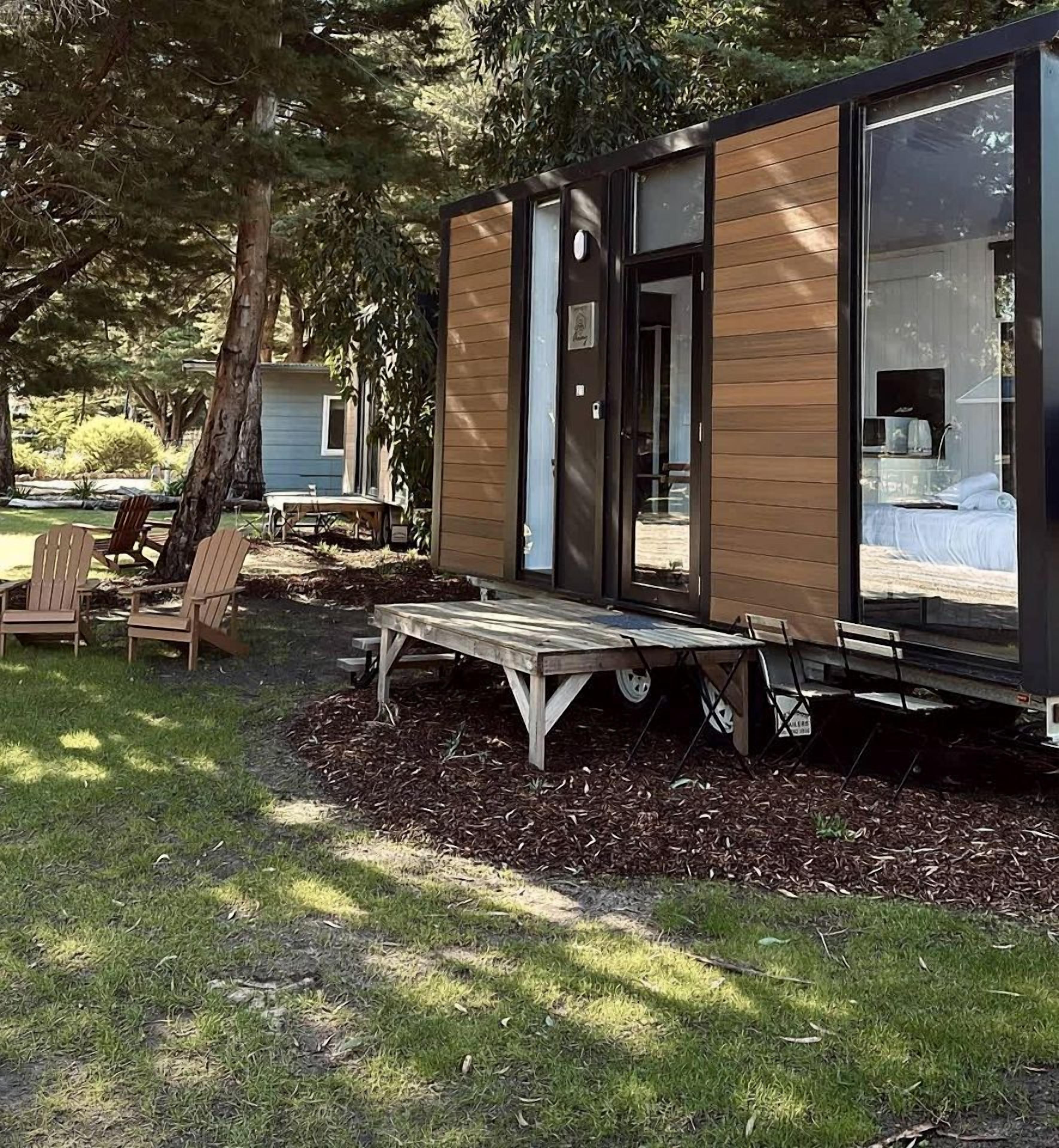A modern, compact cabin with a deck, outdoor seating, and a visible interior with a bed and a bathroom.