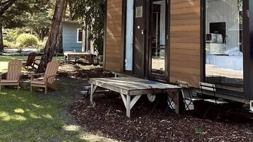 A modern, compact cabin with a deck, outdoor seating, and a visible interior with a bed and a bathroom.
