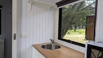A kitchen with a stainless steel sink, wooden countertop, and a window with a view of trees.