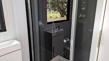 Ein modernes Badezimmer mit Glasabtrennung, einem Waschbecken und einem Fenster.