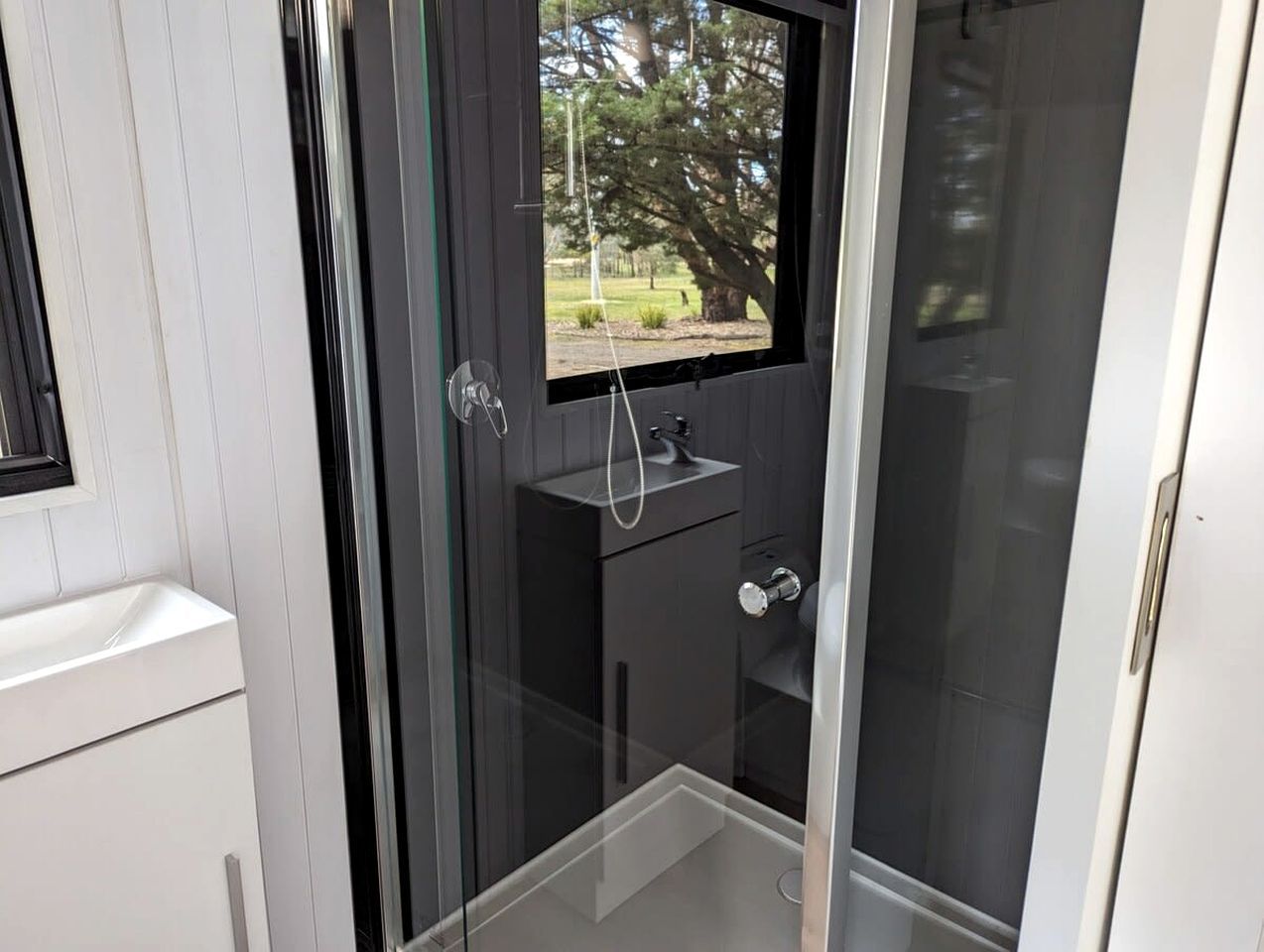 A modern bathroom with a glass enclosure, a sink, and a window.
