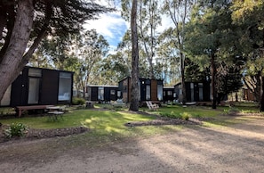 A campsite with multiple cabins, outdoor seating, and a grassy area.