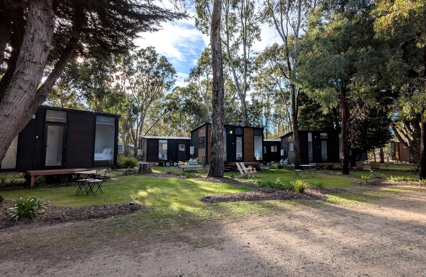 A campsite with multiple cabins, outdoor seating, and a grassy area.