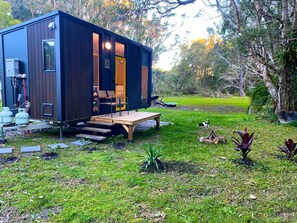 Eine kleine Holzhütte mit einer Terrasse, umgeben von einer Rasenfläche und Bäumen.