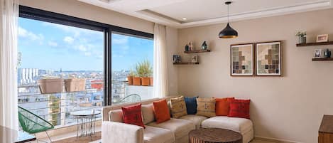 Una sala de estar moderna con un ventanal grande, un sofá modular, una mesa de centro redonda y estantes decorativos.