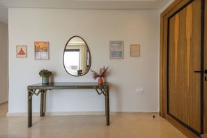 Ein Zimmer mit einem Holzschrank, einem Spiegel, einem Konsolentisch mit einer Topfpflanze und gerahmten Kunstwerken an der Wand.
