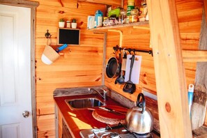 Un interior de madera con una zona de cocina que incluye un lavamanos, un hervidor y diferentes utensilios.