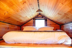 A single bed in a cabin with a sloped ceiling and a window at the peak.