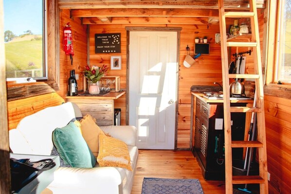 A cozy cabin interior with a wooden interior, a white couch with cushions, a small kitchen area, and a door leading outside.