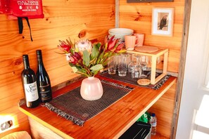 Et barområde i træ med to vinflasker, en vase med blomster og et lille bord med tallerkener og glas.