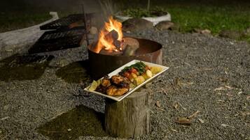 Et lejrbål med en tallerken med grillstegt mad og grøntsager på en træstub.