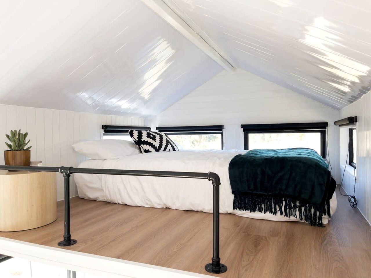Un dormitorio con cama, mesita de noche, planta y ventana.