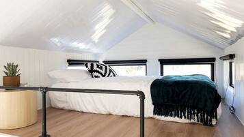 Un dormitorio con cama, mesita de noche, planta y ventana.