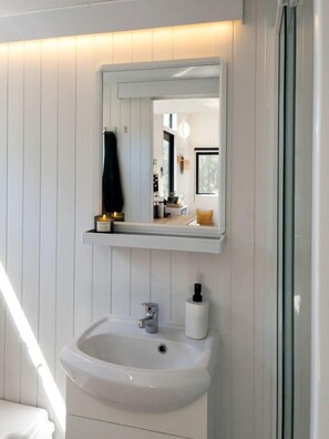 A bathroom with a white sink, a mirror, and a shelf with a candle.