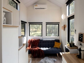Interior acogedor de una cabaña con sofá, una mesita de centro y ventana con vistas al exterior.