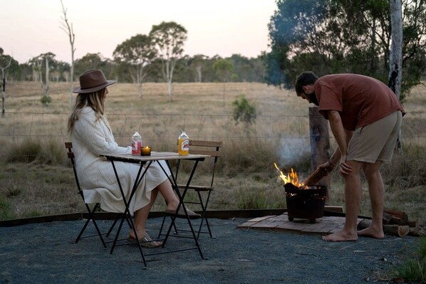 An outdoor dining area with a table and chairs, a fire pit, and a person tending to the fire.