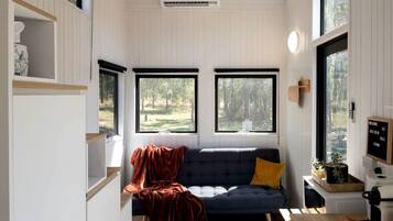 Ein gemütliches Blockhauss-Interieur mit einer Couch, einem Couchtisch und einem Fenster mit Blick ins Freie.