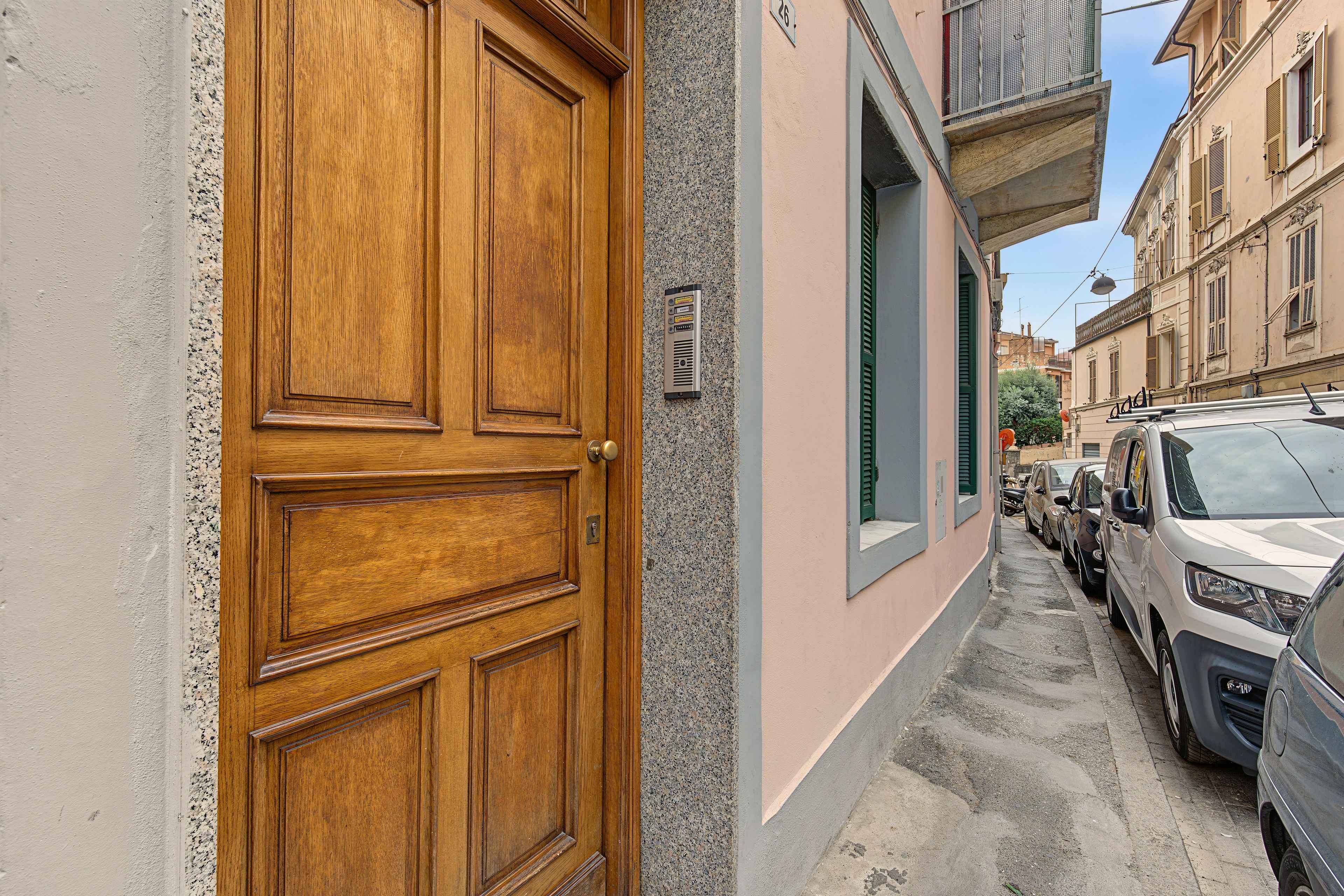 Une rue étroite, bordée de voitures garées, avec une porte en bois sur le côté gauche.