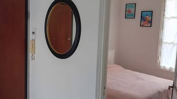 A bedroom with a bed, a door, a mirror, and two wall-mounted pictures.