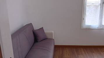 A room with a purple sofa, a framed picture on the wall, and a window with curtains.