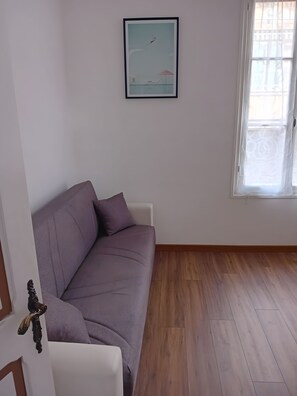 A room with a purple sofa, a framed picture on the wall, and a window with curtains. - Il Gattino di Sanremo 1 – Relaxing Apartment with Wi-Fi, AC & Parking (Sanremo)