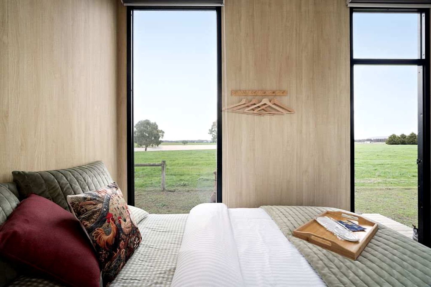 A bedroom with a large bed, a wooden headboard, and a view of a grassy field through a window.