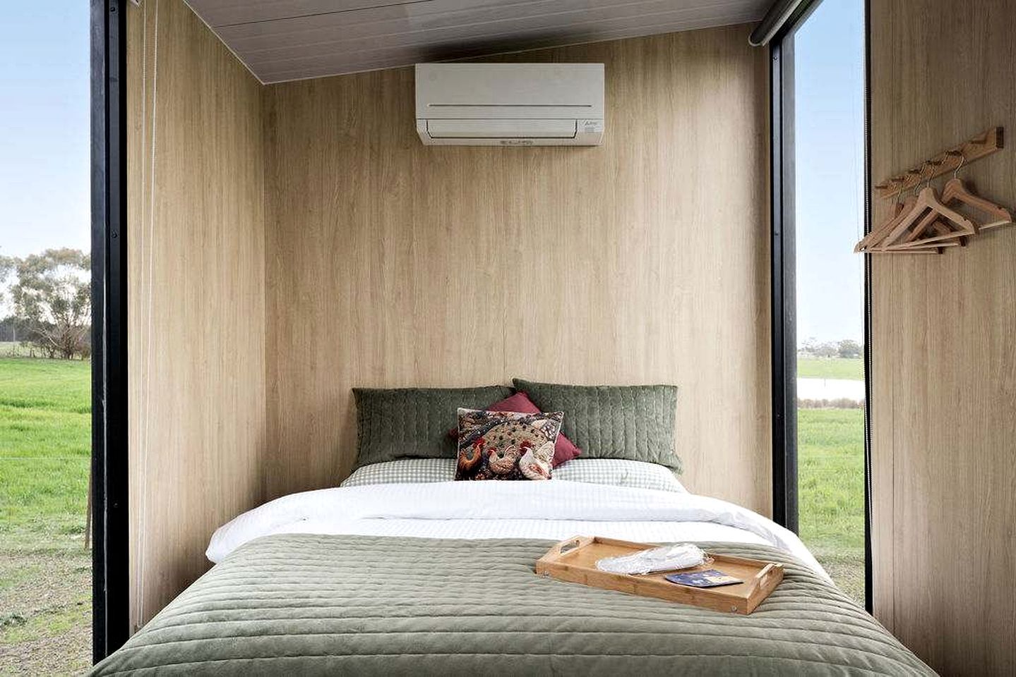 A bedroom with a bed, pillows, a tray, and a view of the outdoors.