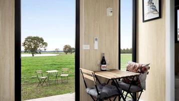 A room with a wooden table and chairs, a bottle of wine, and a view of a grassy field with trees.