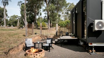 A campsite with a fire pit, outdoor seating, and a trailer with an air conditioning unit.