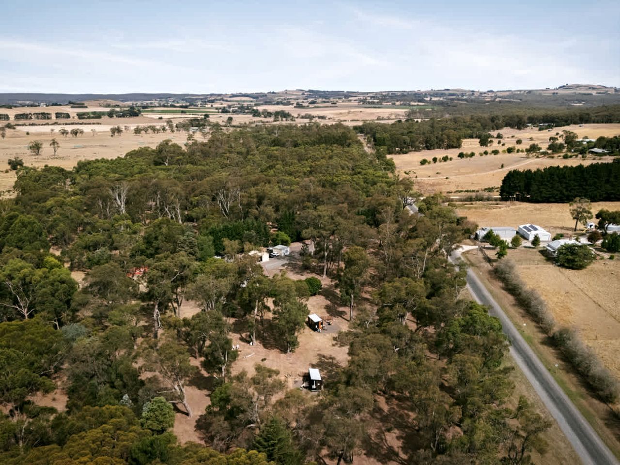 Paisagem rural com edifícios isolados, estrada e vegetação densa.