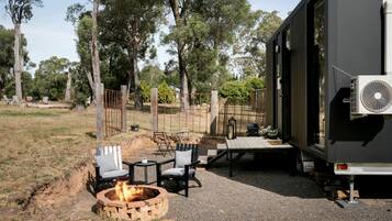 A campsite with a fire pit, outdoor seating, and a trailer with an air conditioning unit.