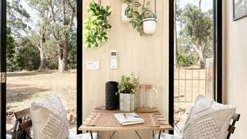 Una habitación con una mesa de madera, dos sillas, una planta colgante y vistas a árboles fuera.