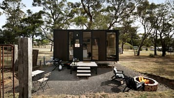 A modern cabin with a patio area, a fire pit, and a dining table.