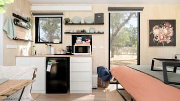 Un espacio habitable compacto con kitchenette, comedor y un amplio ventanal con vistas al exterior.