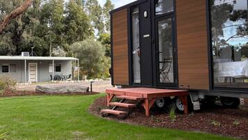A modern mobile home with a large window, a deck, and a small garden area.
