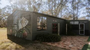 A rustic building with a 'REC ROOM' and 'KITCHEN' labeled, a mural on the side, and a paved entrance area.