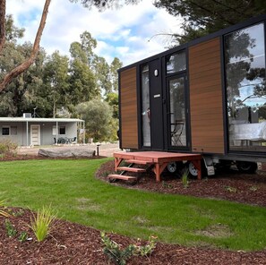 A modern mobile home with a large window, a deck, and a small garden area. - Secluded Tiny House Perfect for Water Activities and Family Escapes in Victoria, Australia (Dadswells Bridge)