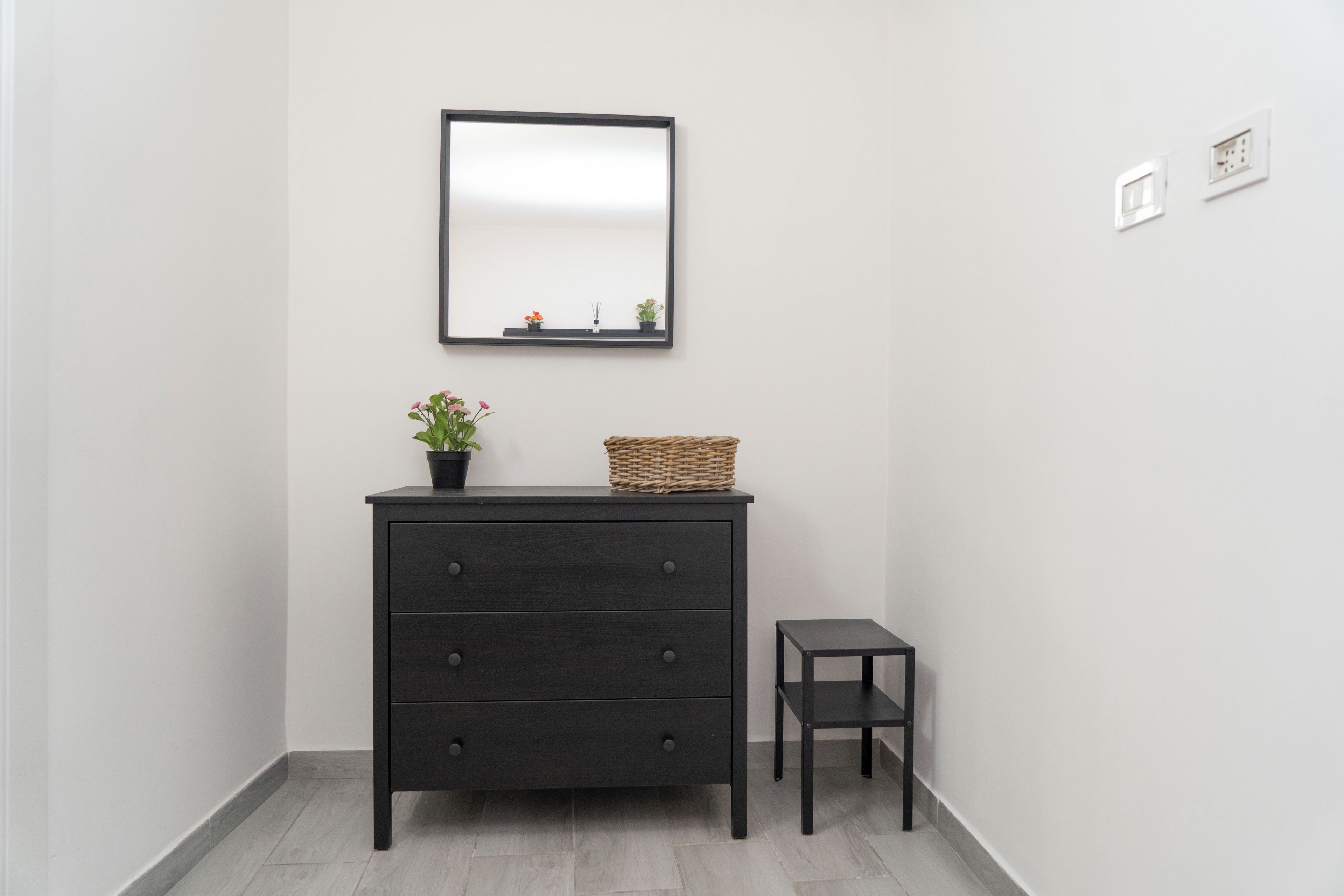 A dark wooden dresser with drawers, a small potted plant, and a wicker basket on top.