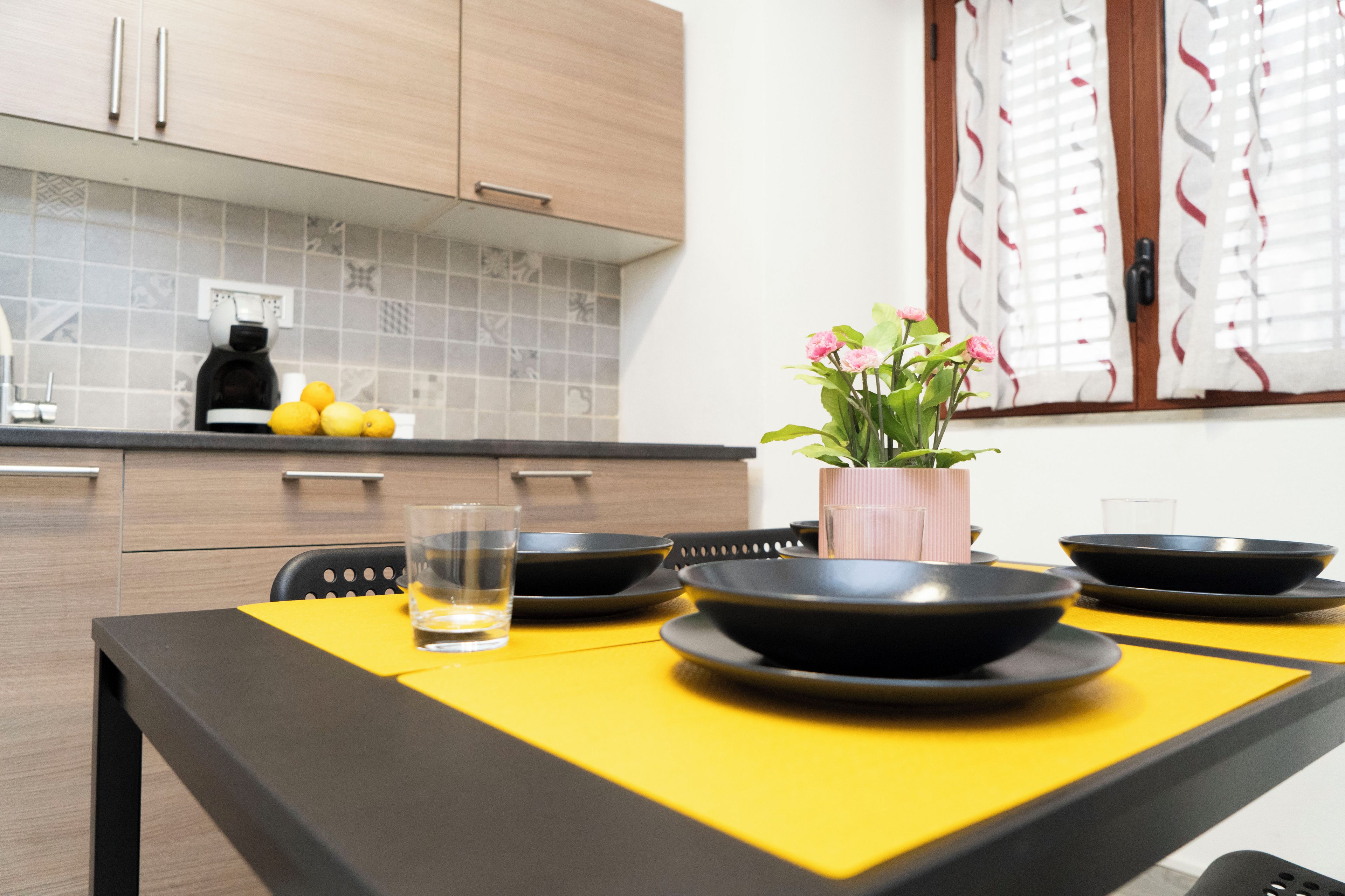 Una cucina moderna con un tavolo da pranzo per quattro persone, con piatti neri e un bicchiere d'acqua.